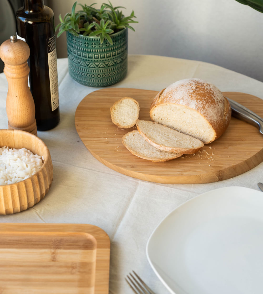 tábua irregular de bambu decorando uma mesa posta com pão e outros alimentos 