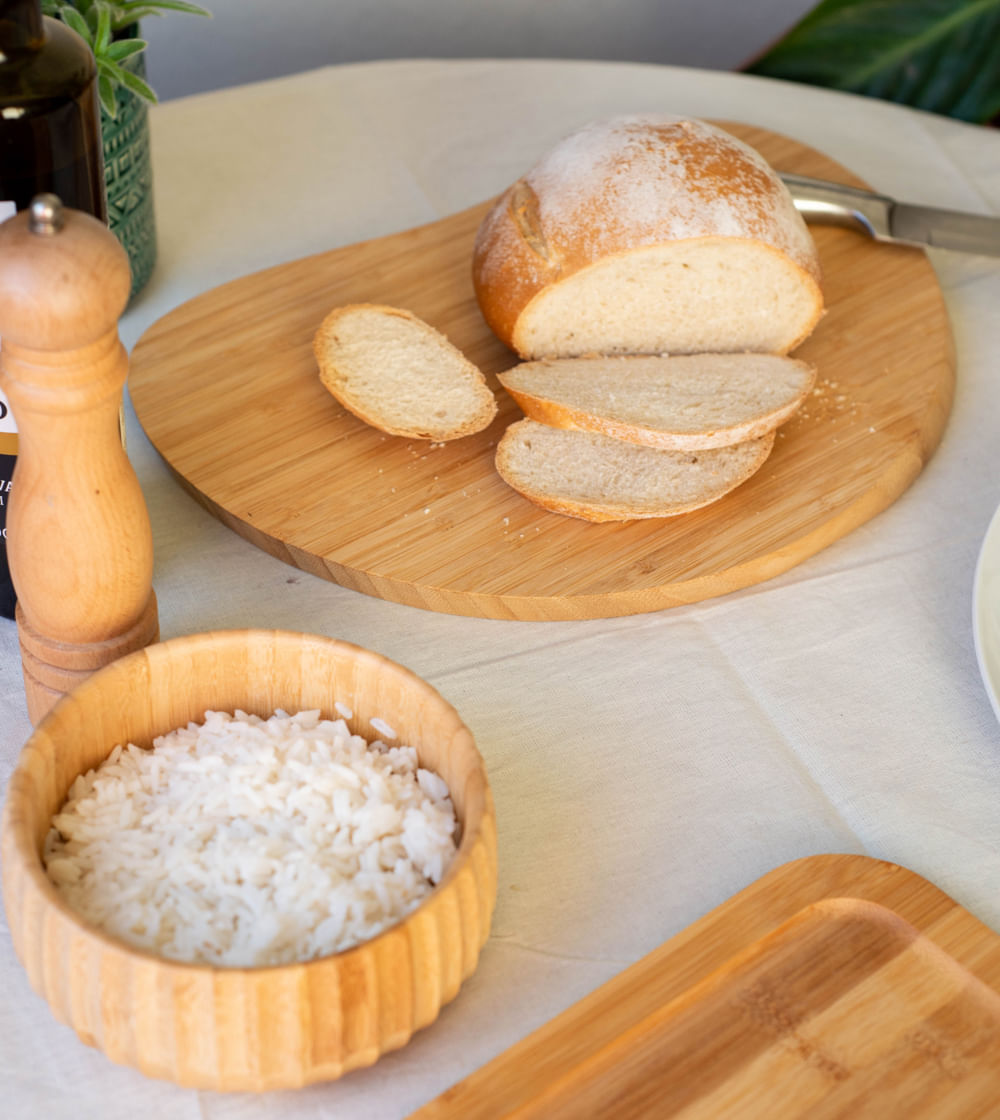 tábua irregular de bambu decorando uma mesa posta com pão e outros alimentos 